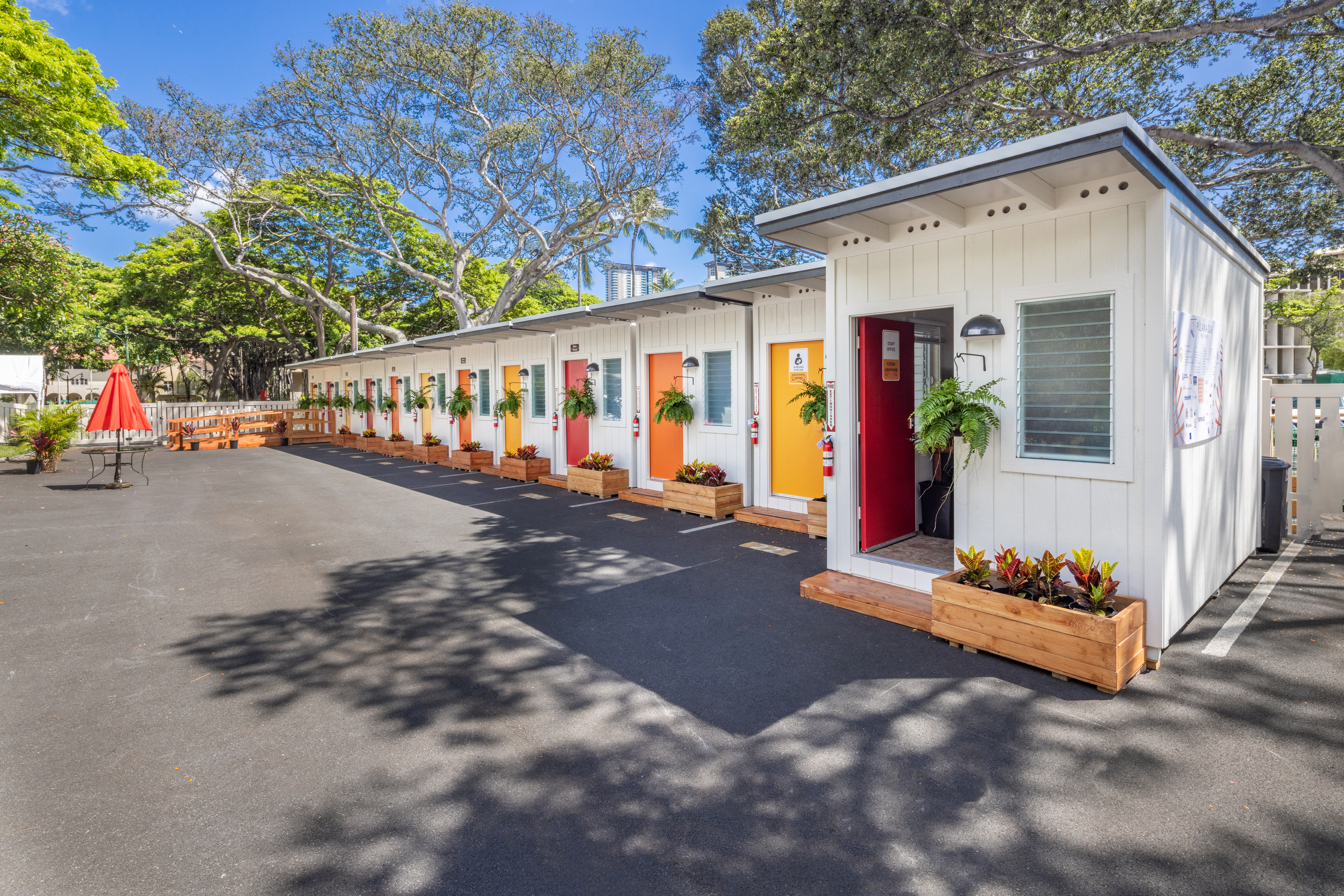 A row of small white pre-fab homes with colorful doors in the sunshine.