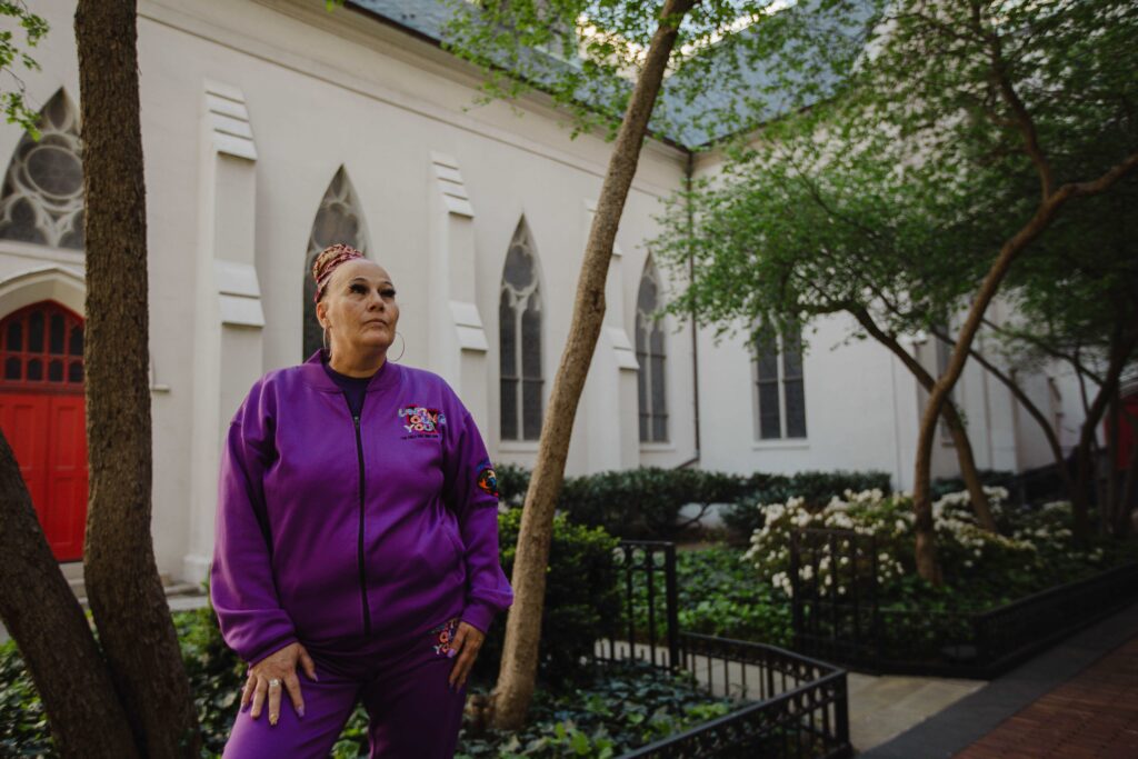 A woman in a purple tracksuit poses in front of a white building.