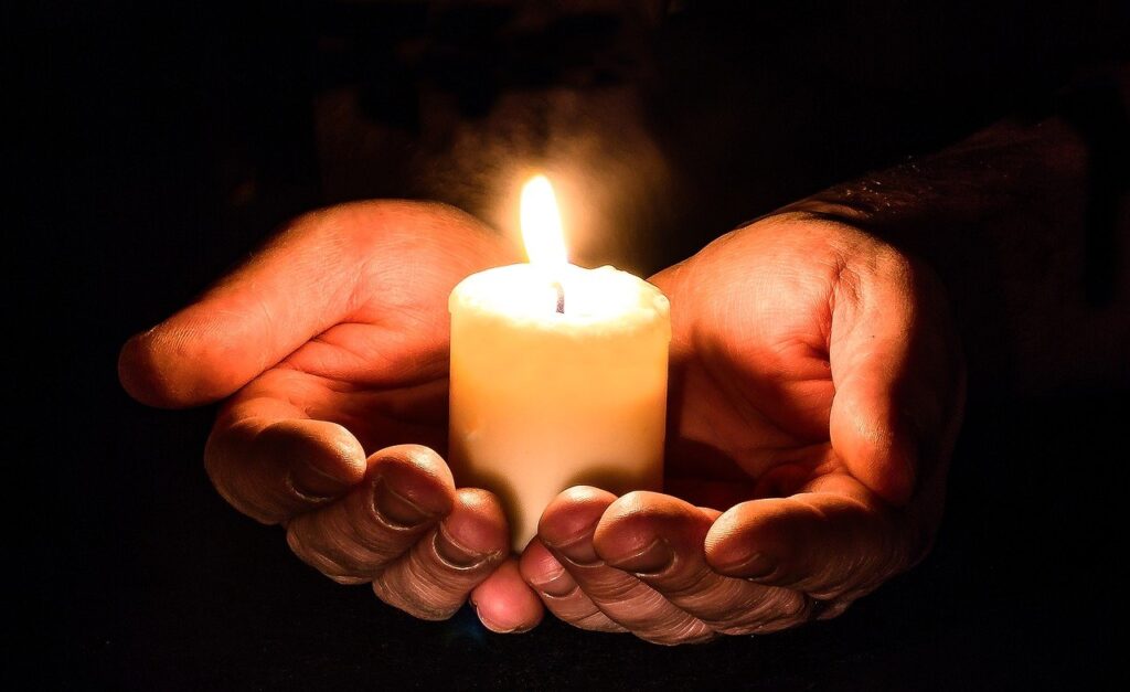Image of outstretched hands holding a single lit candle.