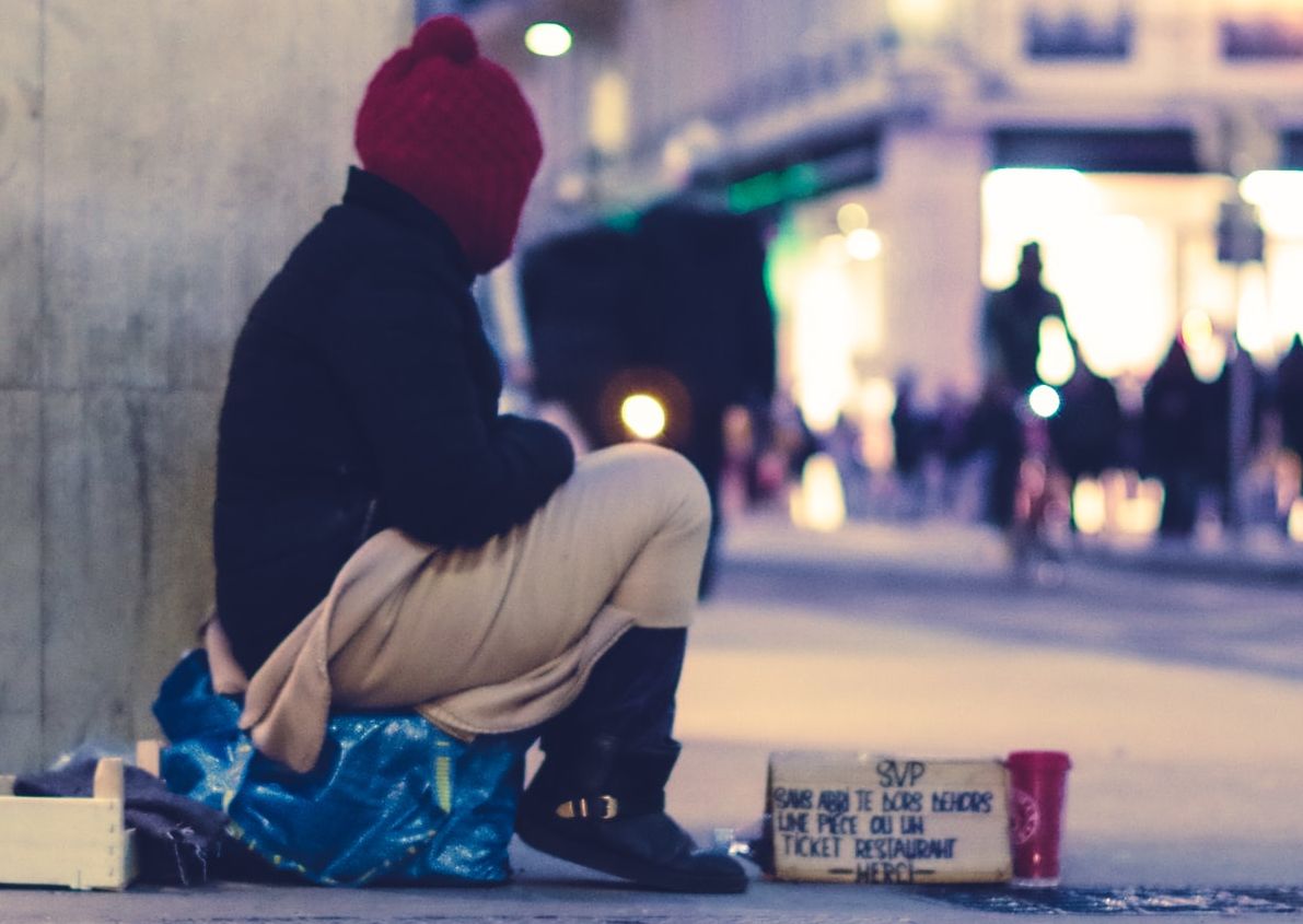 Photo of a bundled up person sitting outside and asking for money.