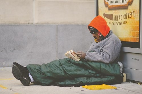 a photo of a homeless man reading a book on the street