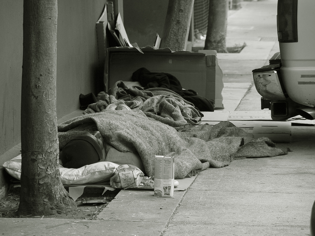 A homeless man sleeps on the sidewalk