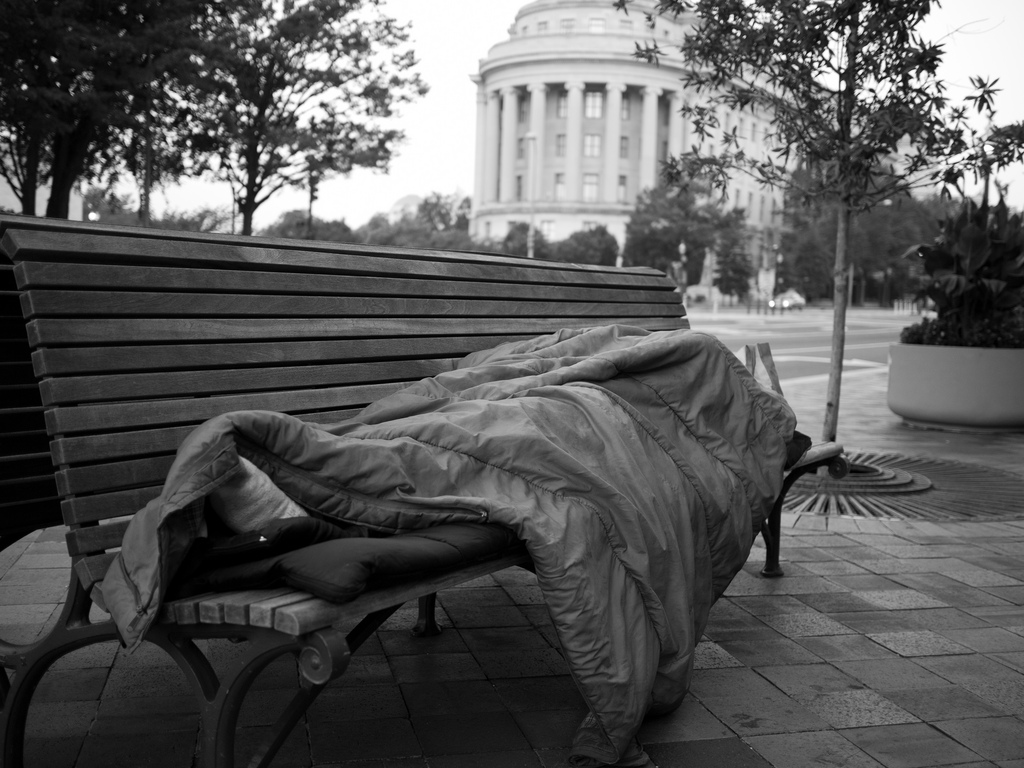 Homeless man sleeps on a sidewalk bench