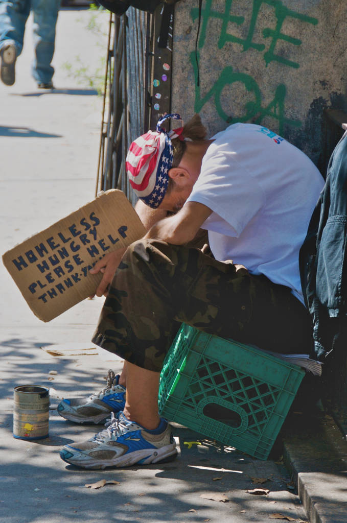A man with a sign saying "Homeless, Please help"