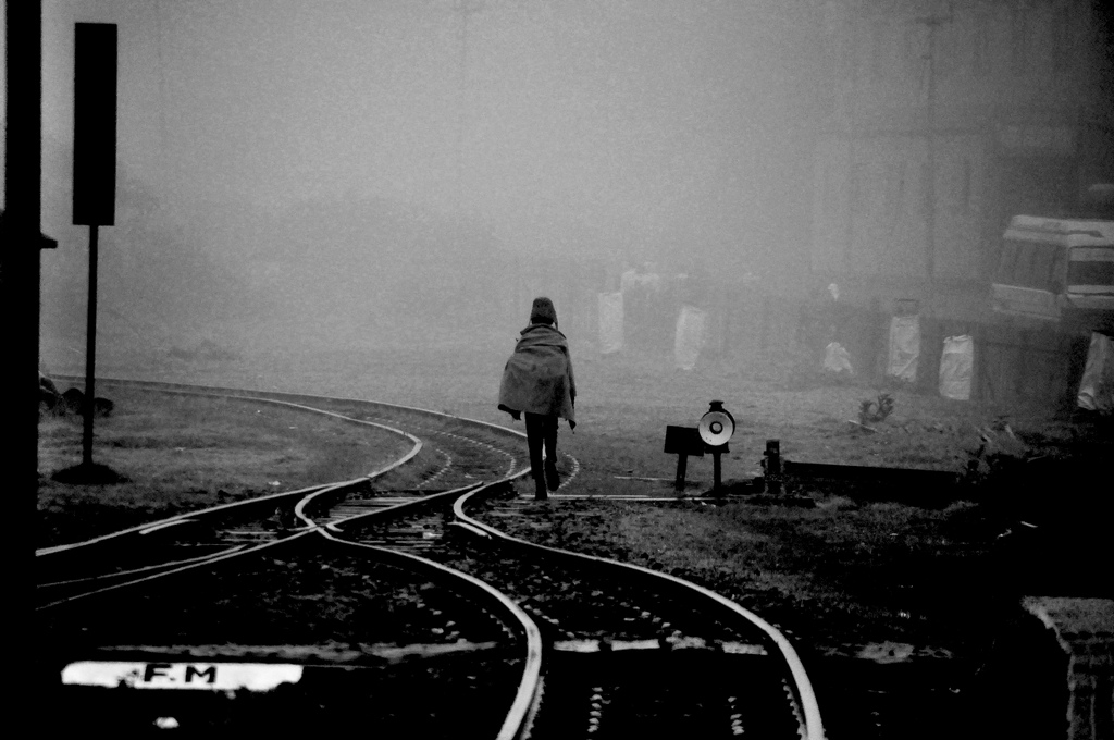 Image of a lone figure walking along a railroad track.
