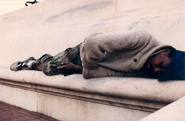 Image of a homeless man sleeping on a bench.