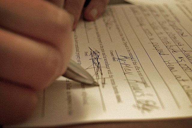 Image of a hand signing a contract.