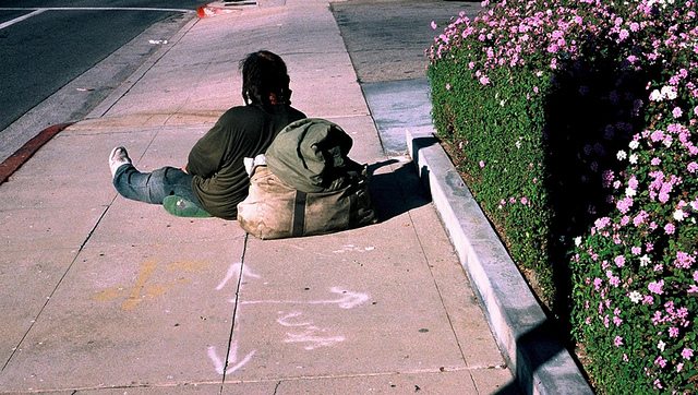 Image of a homeless man sitting on a sidewalk.
