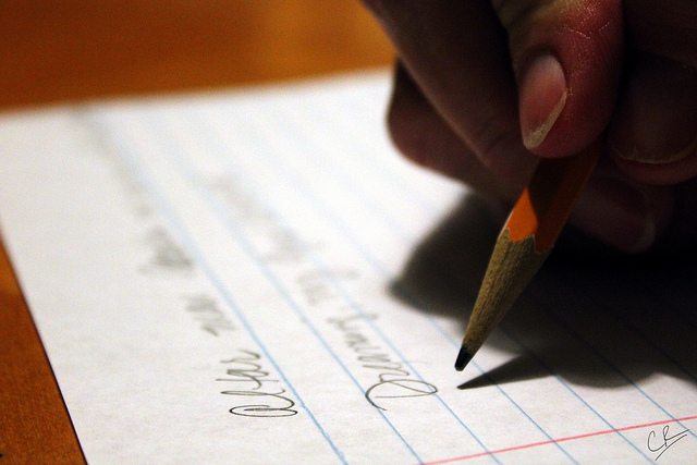 Image of a hand holding a pencil and writing on a piece of paper.