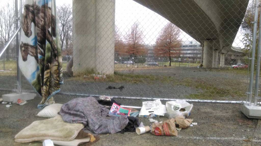 Photo of a blanket hanging off a wire fence post with other belongings scattered on the ground in front of the fence.