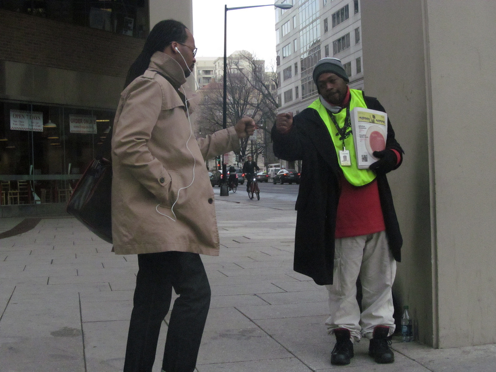 A picture of a Street Sense vendor and customer fist bumping on a city street.