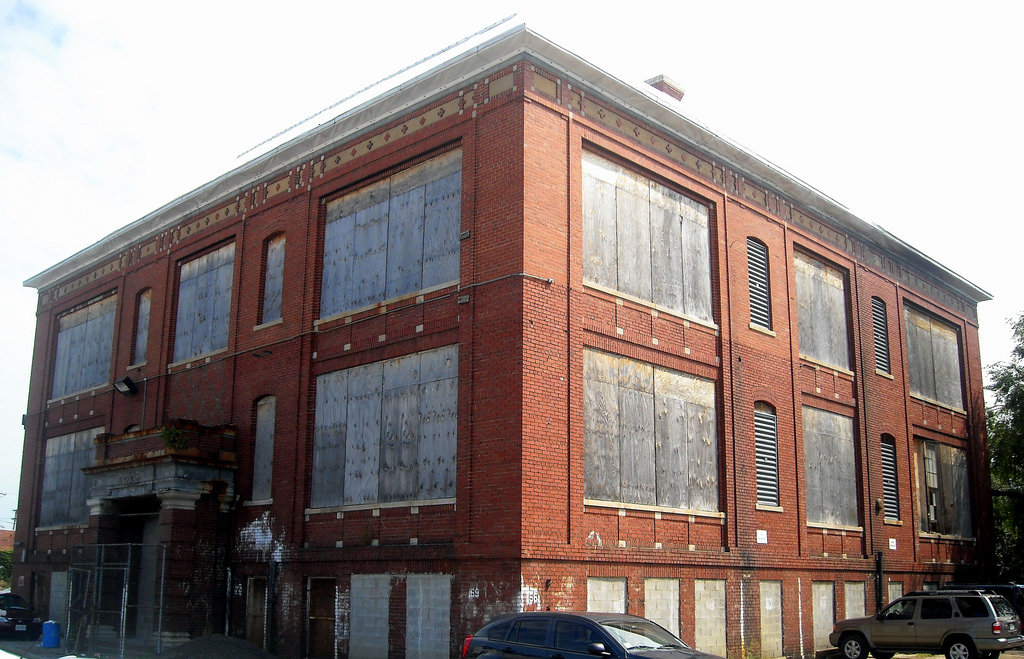 A two story red brick building with boarded up windows.