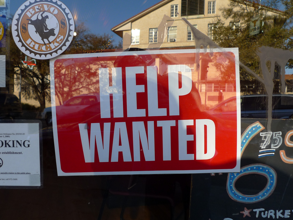 A "help wanted" sign hangs outside an establishment.