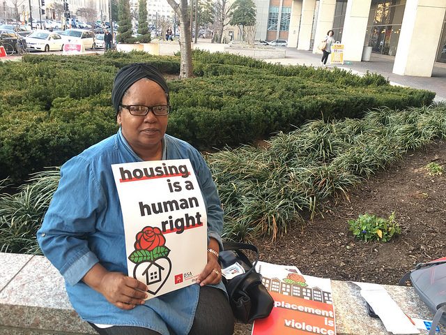 Woman at the protest holds a sign that reads, "Housing is a Human Right".