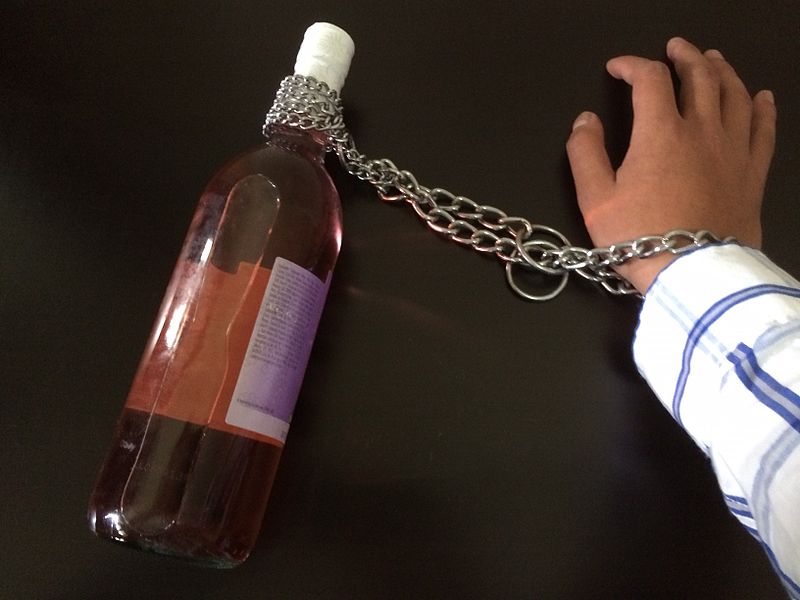 A photo of a hand chained to a bottle of Alcohol.