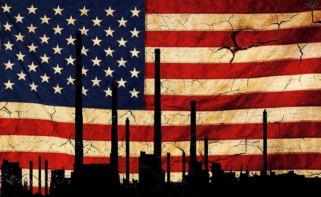 Silhouette of industrial buildings against a backdrop wall of a cracking American flag