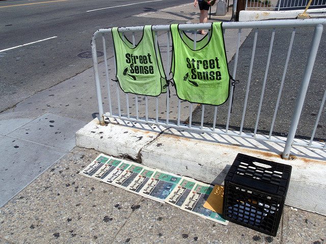 Street Sense vendor vests hang above newspapers lined up on a sidewalk.