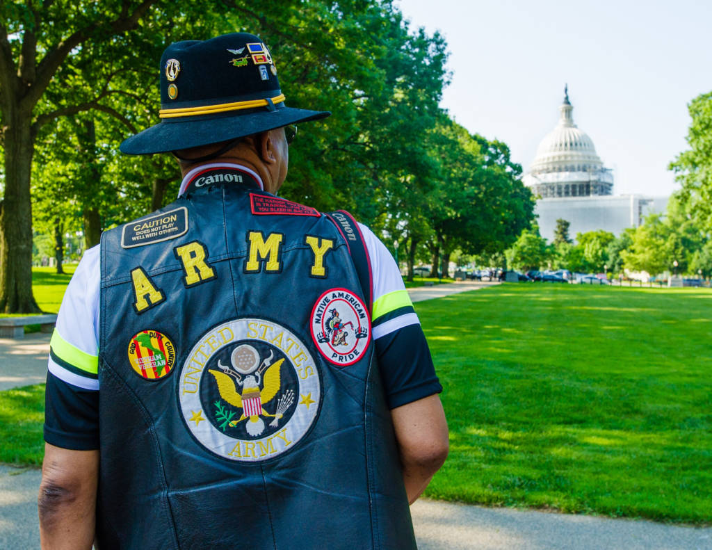 Photo of a man in a jacket that says "Army" standing with the U.S. Capitol in front of him.