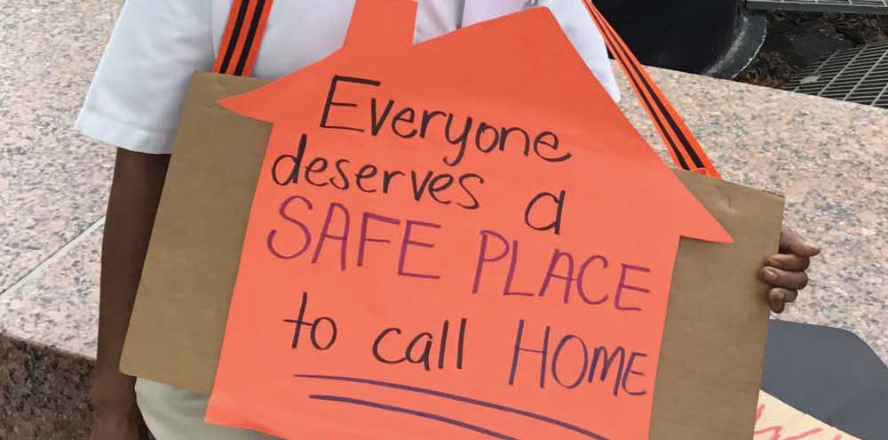 A photo of a man holding a sign saying "Everyone deserves a safe place to call home."