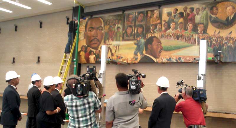 Officials and journalists watch as the Martin Luther King Jr. mural is lowered from the wall at the downtown DC library.