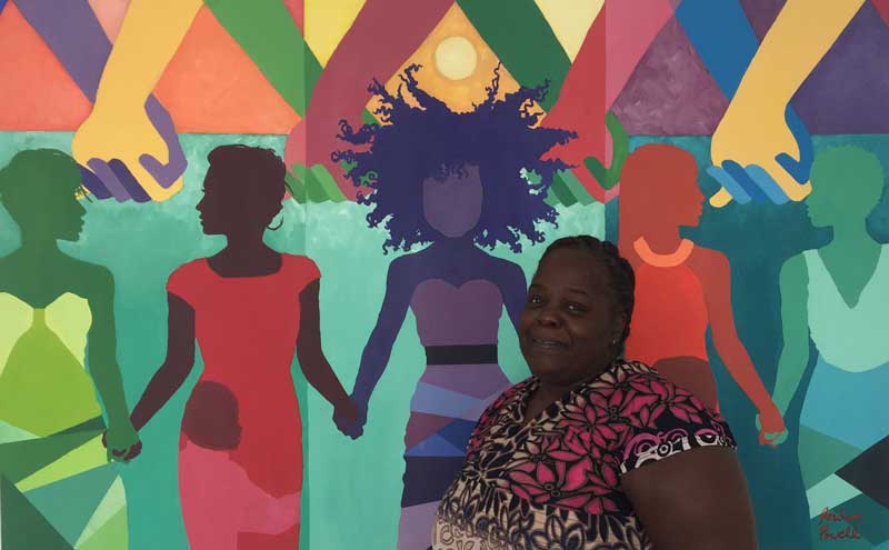 Charlene Davis stands in front of a colorful mural at New Endeavors by Women that was painted by local artist Jordan Powell.