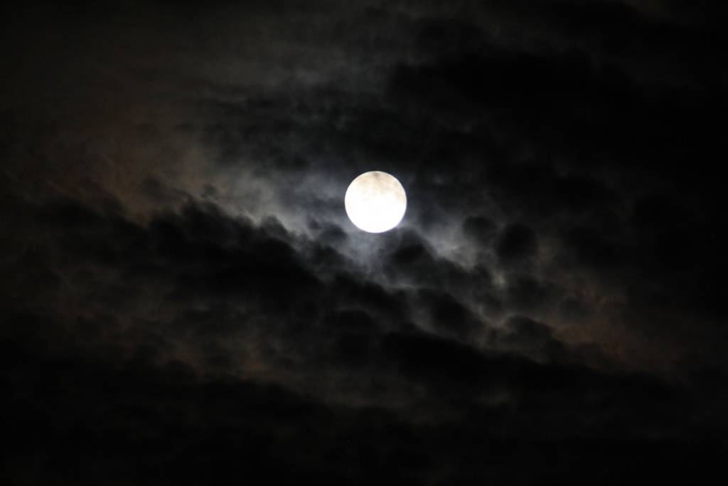 A photo of midnight sky with the moon behind clouds.