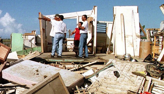 Four men stand amidst a hurricane-destroyed home