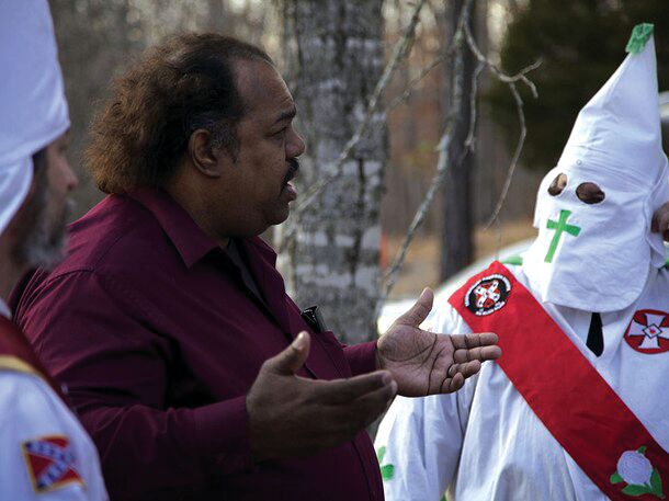 A man in plain clothes talking to someone in a KKK robe
