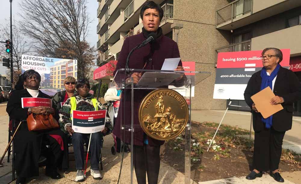 Mayor Bowser stands at a podium, flanked by senior housing residents and Councilmember Bonds.