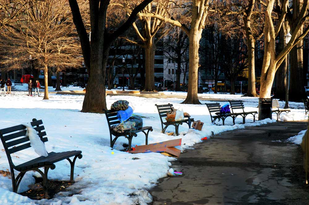 Photo of Franklin Square Park pathway and benches. Snow covers the ground and people's things are sitting on benches.