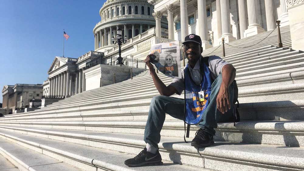 A street paper vendor sitting on the steps of the U.S. capitol building.