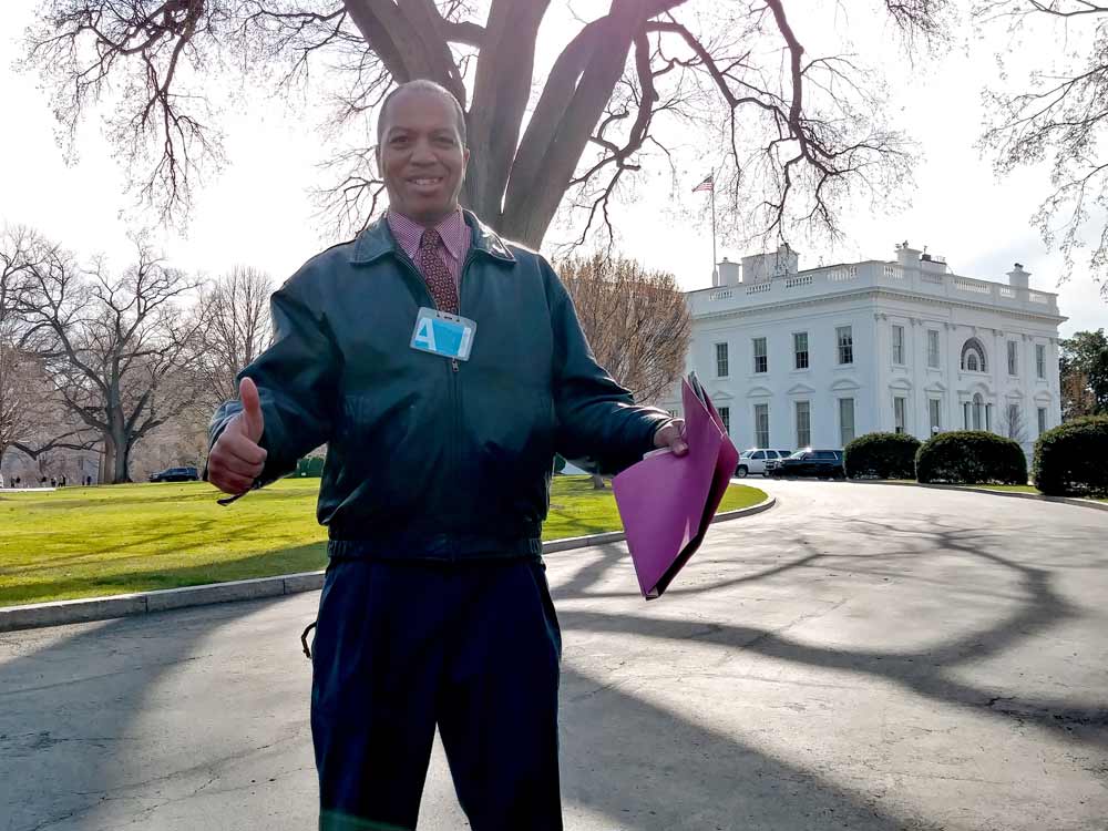 Jeff McNeil, holding a folder with some of his printed articles, standing in front of the White House, past security.