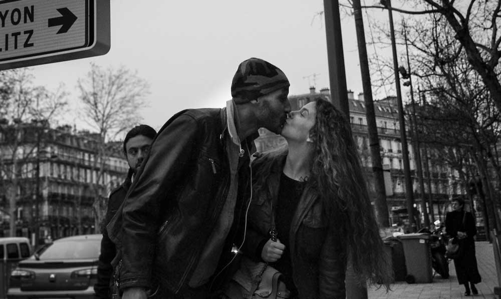 A black and white photo of a young couple hugging on a public street.