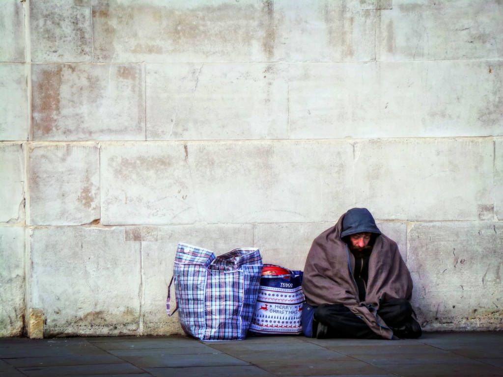 A homeless man sits bundled up against a wall.