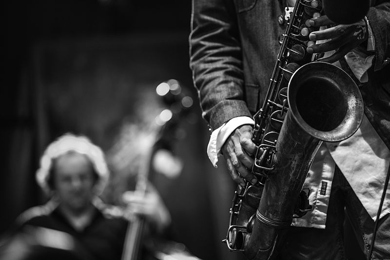 A close up of a man playing a saxophone while a jazz band plays in the background
