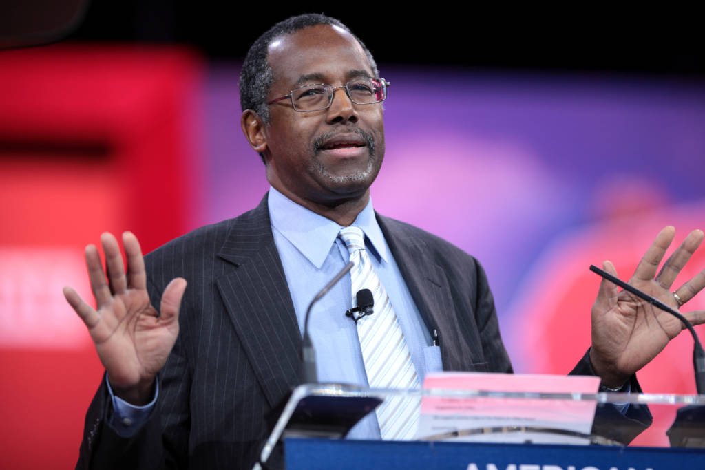 Ben Carson speaking at a podium with his arms outstretched