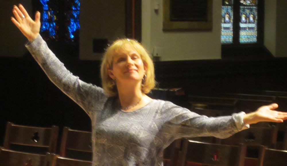Photo of a woman with her arms outstretched in both directions, as if singing or spinning in a dance.