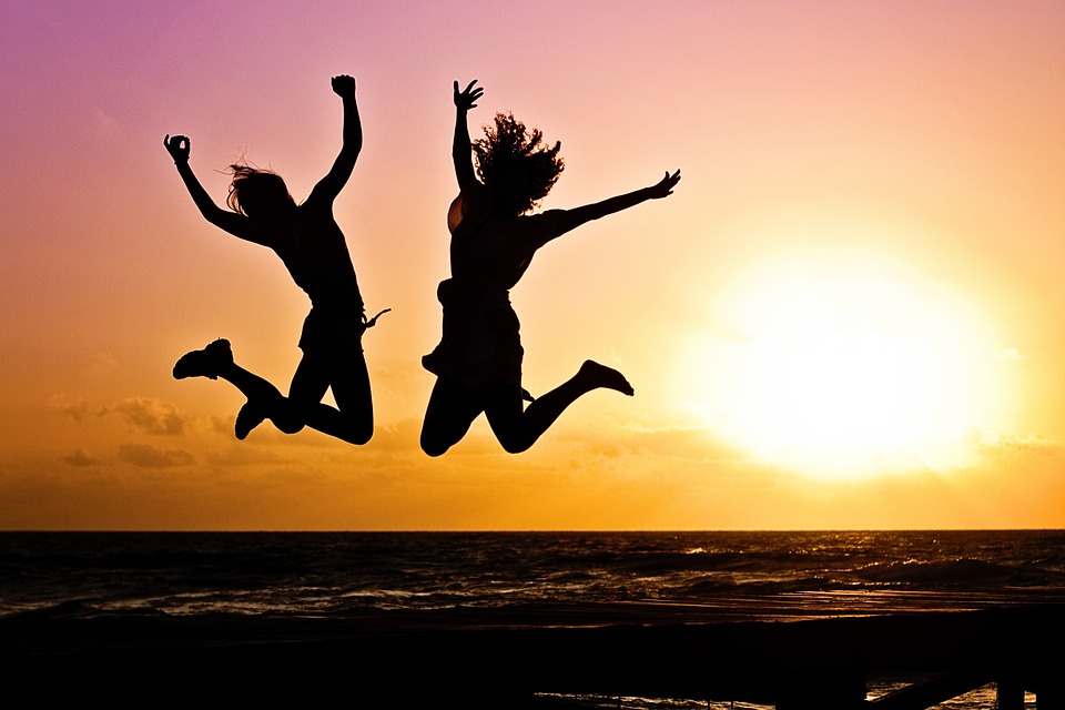 Two young people jumping in the air in front of sunrise.