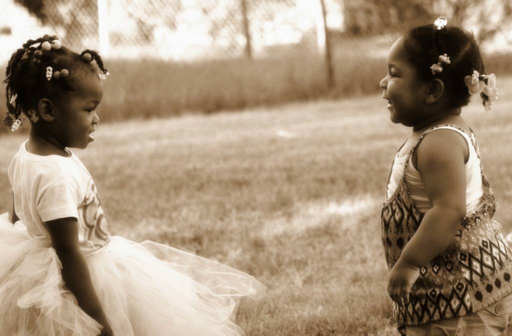 Two little girls in pretty dresses playing in a field.
