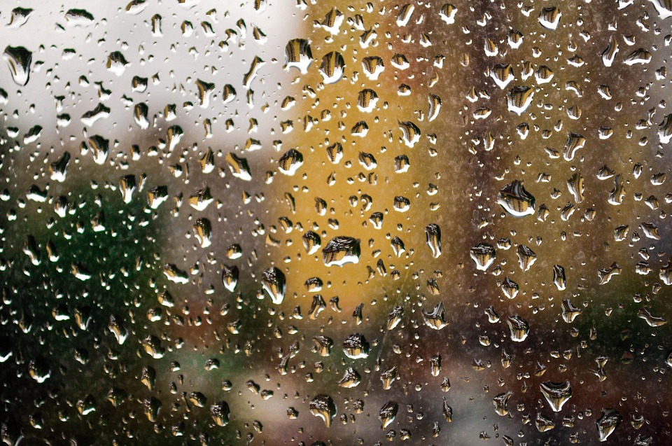 A photograph of a rain-covered window, with blurry images f buildings beyond.