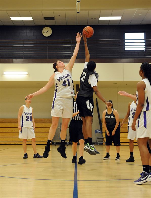 A photograph of women playing basketball, in which two are jumping for the ball.