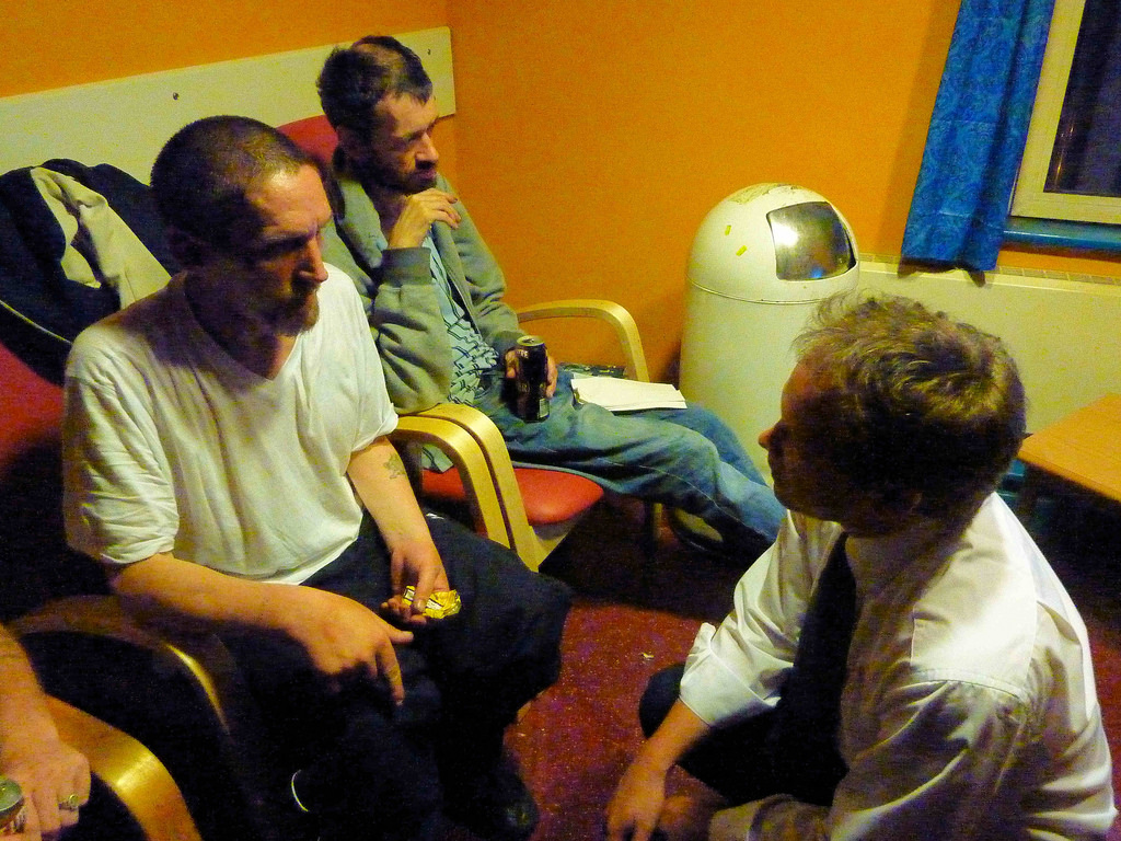 A photograph of one man talking to two others in a homeless shelter.