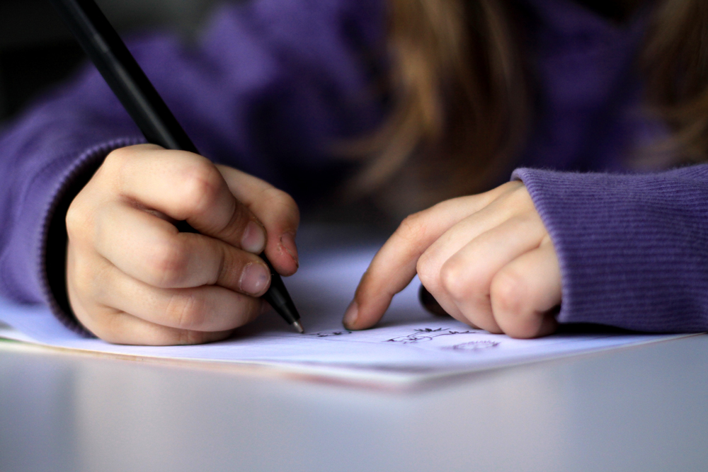 Photo of child wearing purple shirt writing on a piece of paper