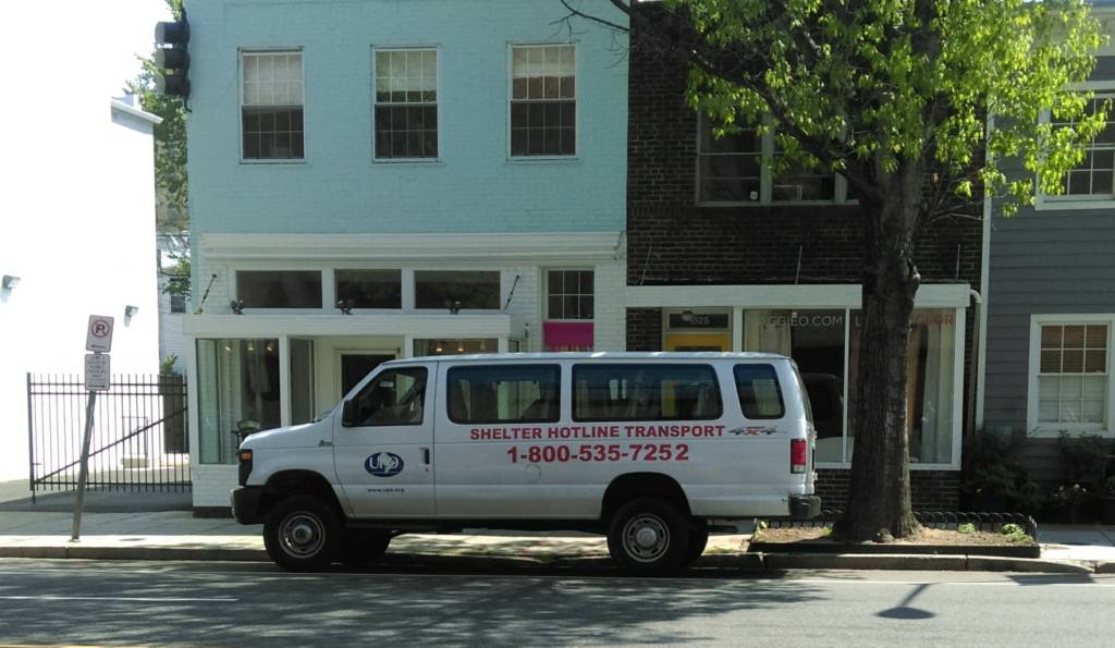 A white van on 14th St. NW with the letters "Shelter Hotline Transport: 1-800-535-7252" painted in red on the side.