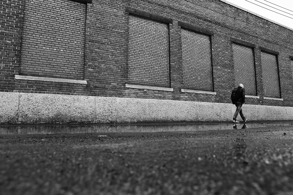 A photograph of a man walking past an industrial building.