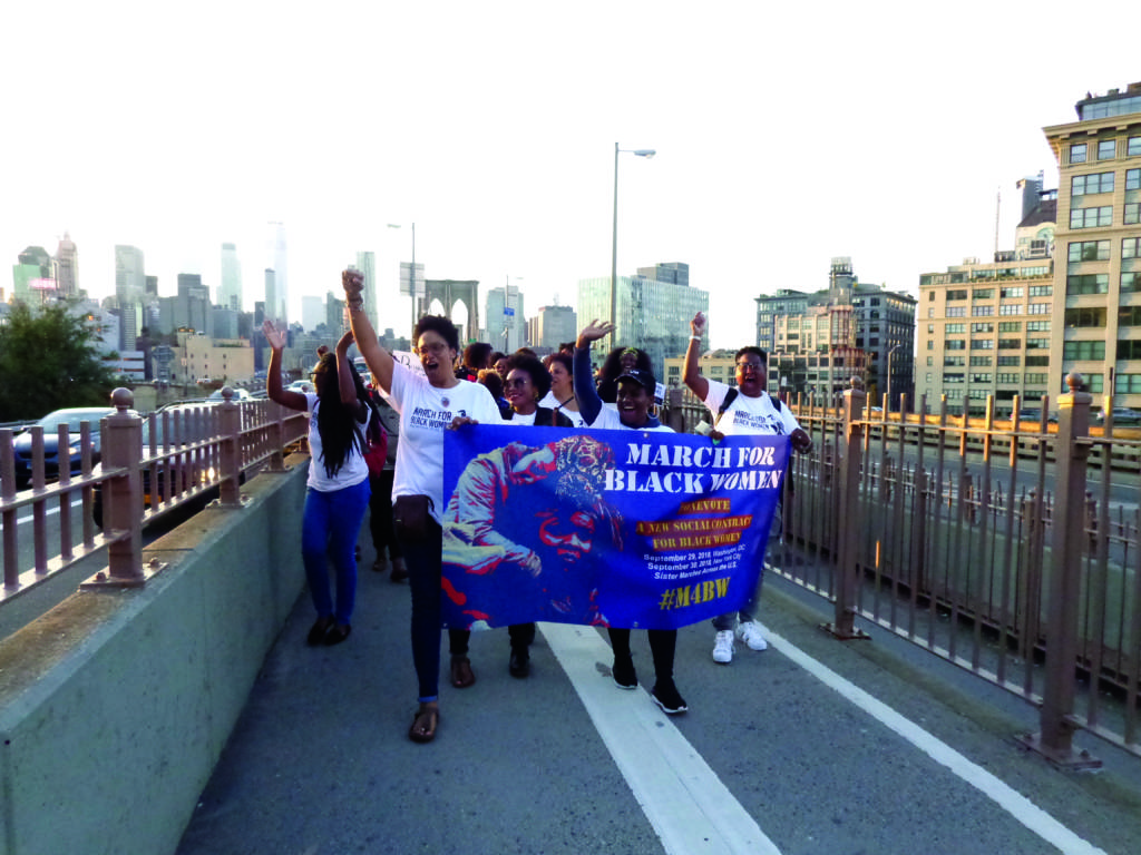 A photograph of people marching across the Brooklyn Bridge carrying a banner that reads "March For Black Women."