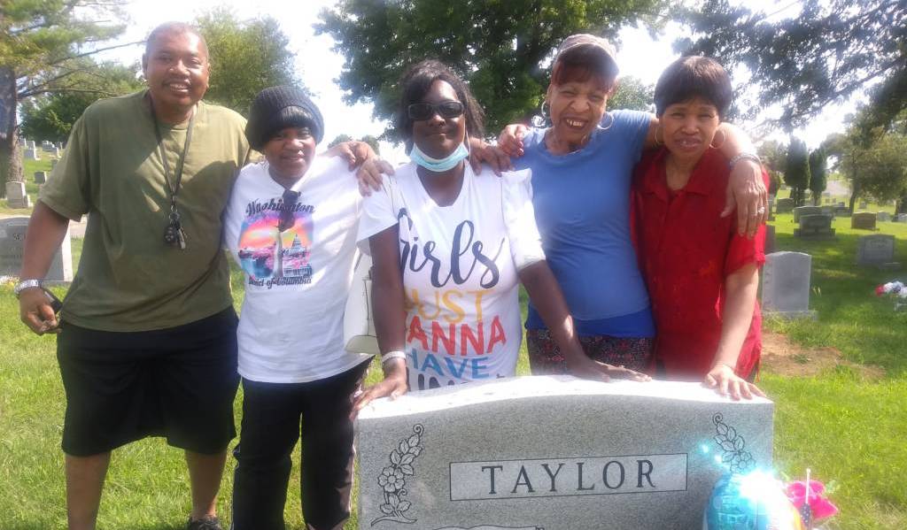 Sybil Taylor stands with family next to her father's grave in a cemetery.