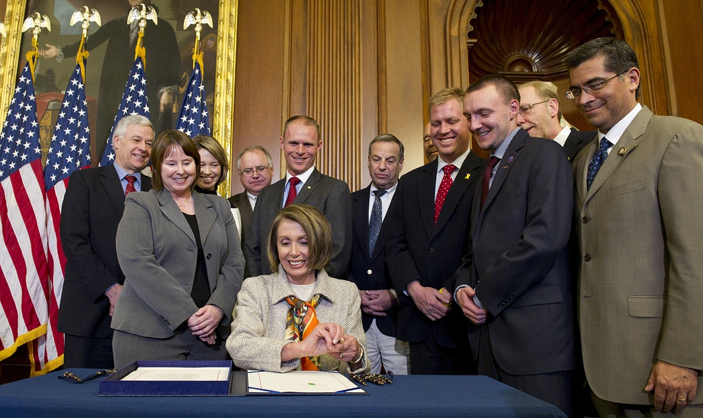A photograph of House Democratic leader Nancy Pelosi seated and surrounded by colleagues.