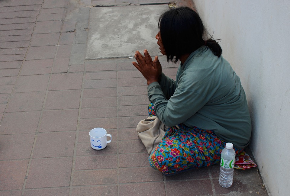 A photograph of a homeless woman sitting on the sidewalk next to a bottle of water.