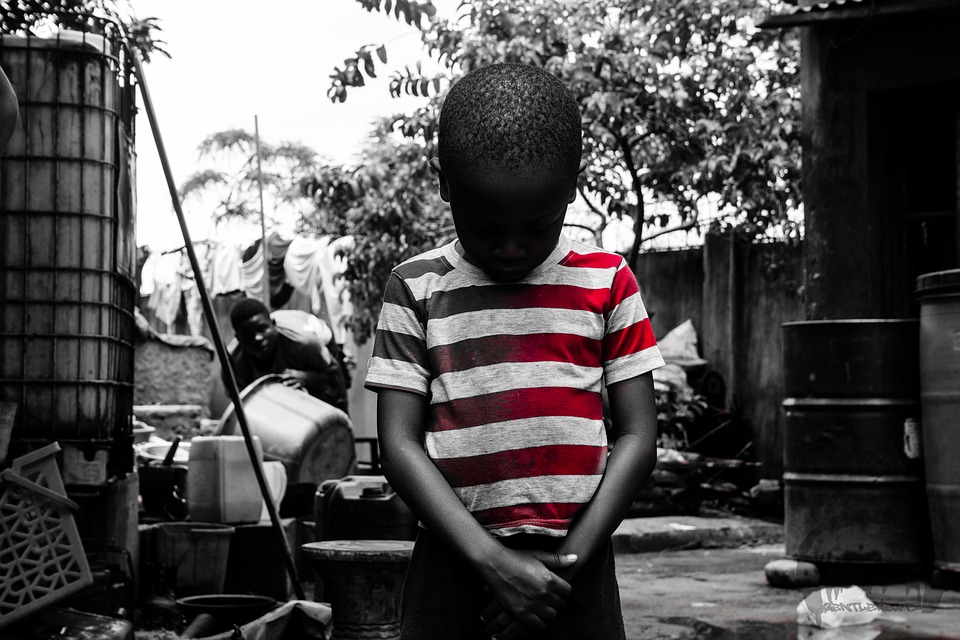 Photograph of a boy in a striped shirt, staring at the ground.